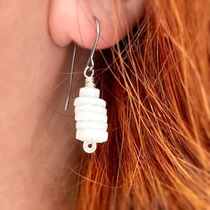 May include: White dangle earrings with a stack of small, round, white beads. The beads are stacked on a silver wire and hang from a silver hook.