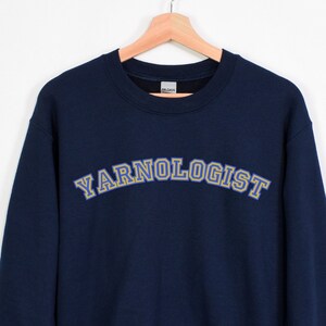 May include: A navy blue sweatshirt with the text "YARNOLOGIST" in yellow and blue lettering.