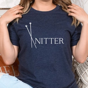 May include: A navy blue t-shirt with a white graphic of knitting needles and the word "Knitter".