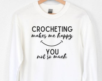 May include: White long-sleeved sweatshirt with black text that reads "Crocheting makes me happy, you not so much" with a smiley face graphic.