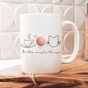 May include: White ceramic mug with a black outline of a cup of coffee, yarn with knitting needles, and a cat's face. The text "It's the simple things" is printed below the images.