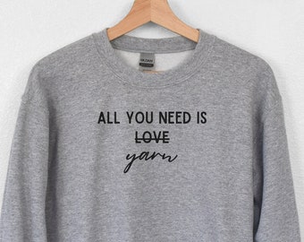 May include: Gray sweatshirt with the text "All you need is love yarn" in black.