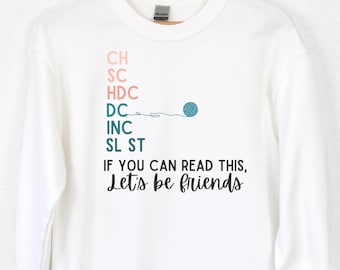 May include: White sweatshirt with a crocheting themed design. The text reads "CH SC HDC DC INC SL ST IF YOU CAN READ THIS, Let's be friends".
