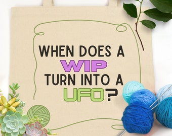May include: A beige tote bag with the text "When does a WIP turn into a UFO?" printed on it. The text "WIP" is in purple and the text "UFO" is in green. The bag is surrounded by yarn balls and knitting needles.
