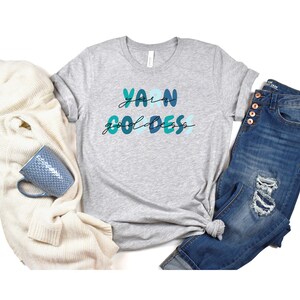 May include: Gray t-shirt with the text "Yarn Goddess" in blue and green lettering.