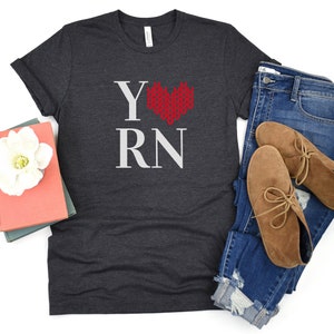 May include: A dark gray t-shirt with the text "Y RN" in white and a red knitted heart in the center.