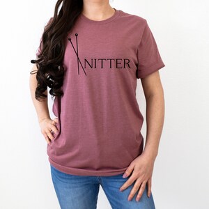 May include: A mauve t-shirt with a graphic of knitting needles and the word "Knitter" printed on the front.