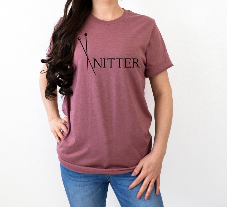 May include: A mauve t-shirt with a graphic of knitting needles and the word "Knitter" printed on the front.
