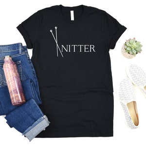 May include: Black t-shirt with white text that says "Knitter" and a graphic of two knitting needles.