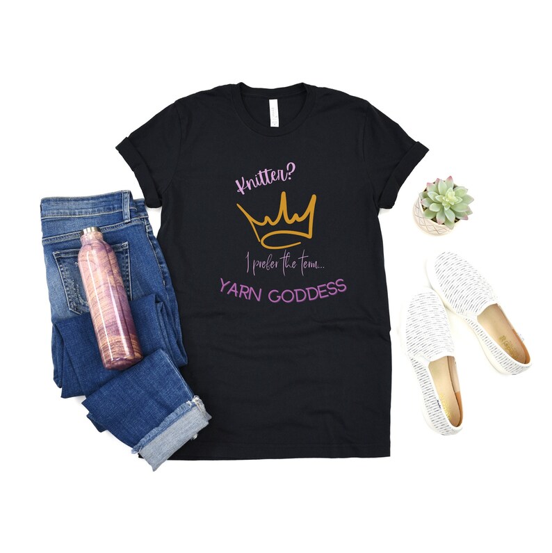 May include: Black t-shirt with a gold crown and the text "Knitter? I prefer the term... YARN GODDESS" in pink and gold lettering.