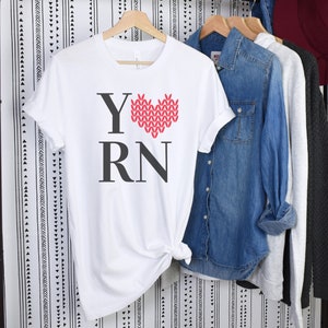 May include: White t-shirt with a red knitted heart and the text "Y RN" printed on the front.
