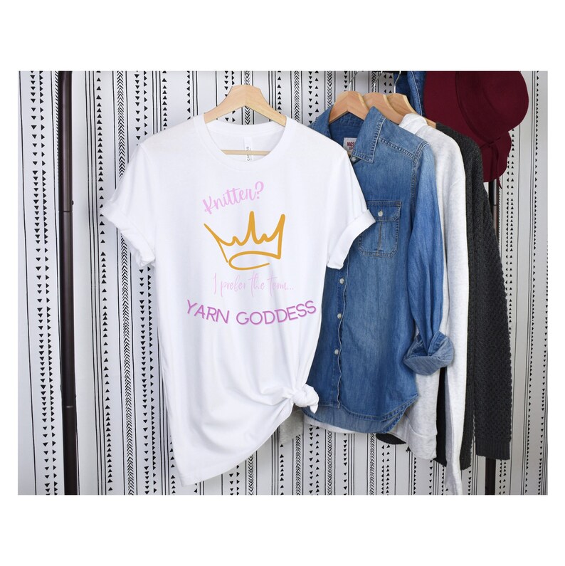 May include: White t-shirt with a pink and gold crown graphic and the text "Knitten? I prefer the term YARN GODDESS".