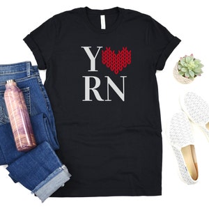May include: Black t-shirt with a white graphic that says "Y" with a red knitted heart and "RN".