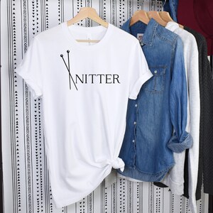 May include: White t-shirt with black text that reads "Knitter" and a graphic of two knitting needles.