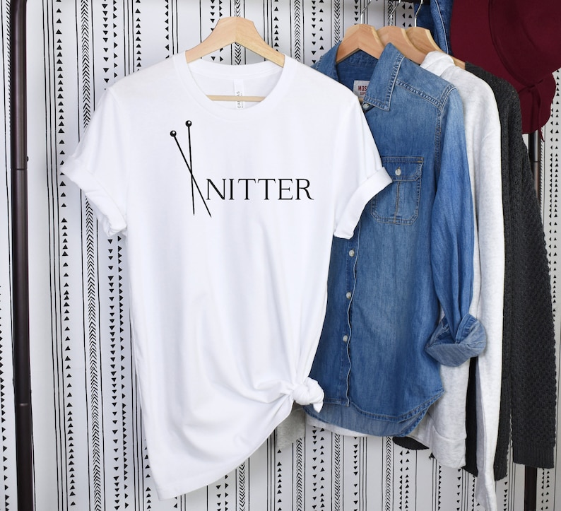 May include: White t-shirt with black text that reads "Knitter" and a graphic of two knitting needles.