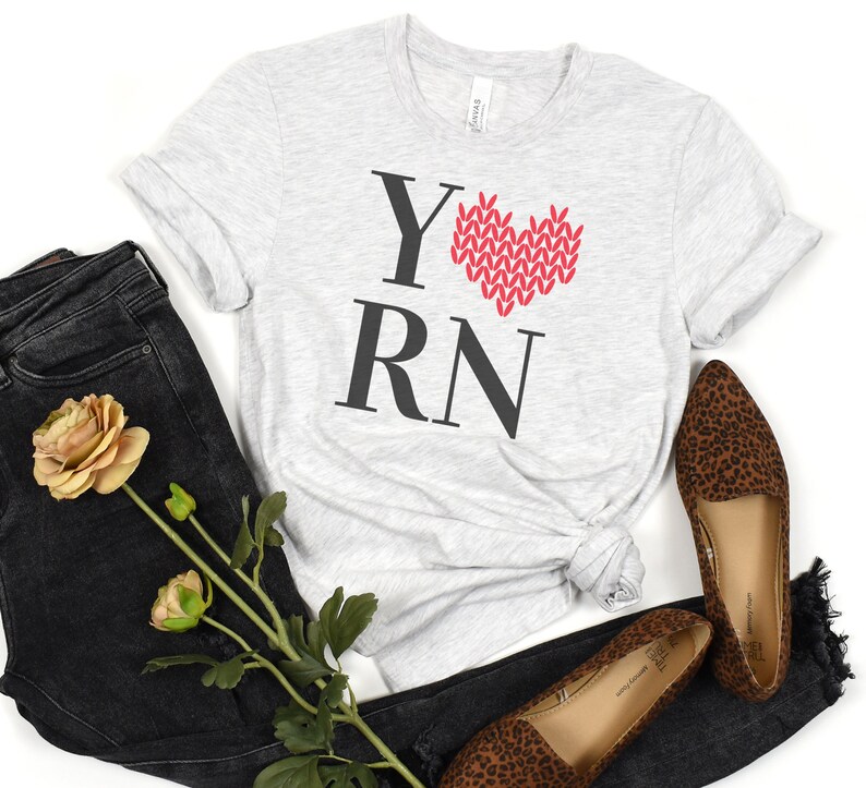 May include: A gray t-shirt with the text "YRN" in black letters and a red knitted heart in the center. The heart is made of yarn and has a white outline.