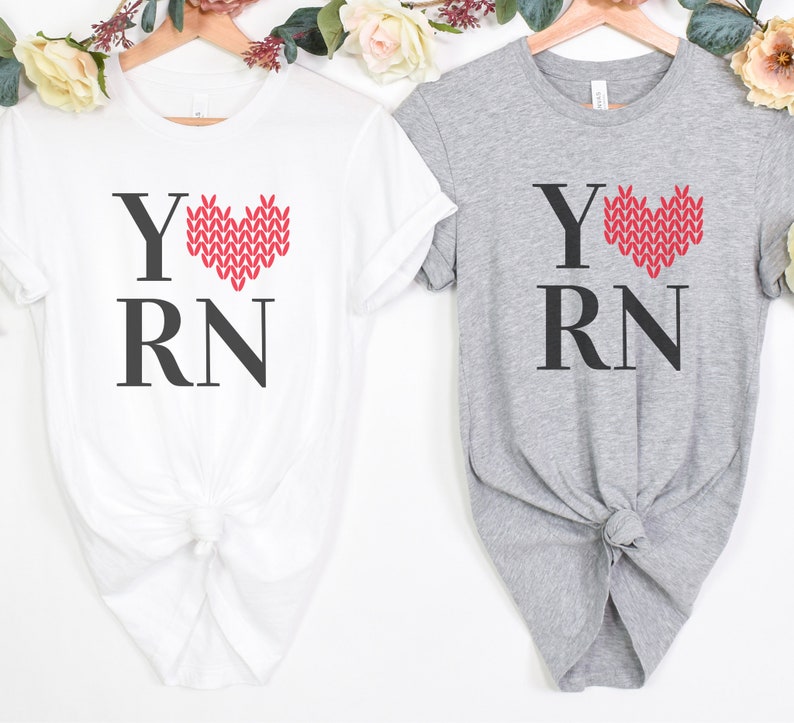 May include: Two t-shirts with the text "Y RN" and a red knitted heart. The heart is a stylized representation of a knitted stitch. One shirt is white and the other is gray.