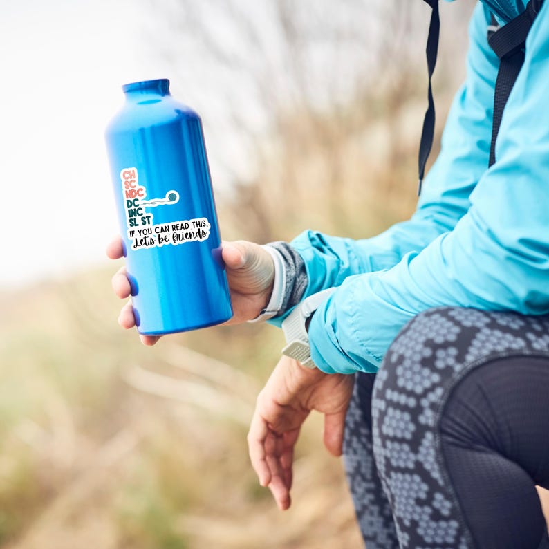 May include: A blue water bottle with a sticker that reads "If you can read this, Let's be friends." The bottle is held by a person wearing a blue jacket. The background is blurred, suggesting an outdoor setting.