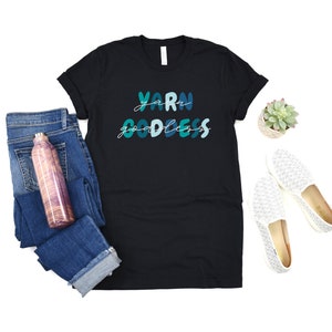 May include: Black t-shirt with the text "Yarn Goddess" in blue and green lettering.