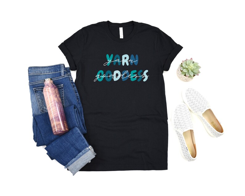 May include: Black t-shirt with the text "Yarn Goddess" in blue and green lettering.