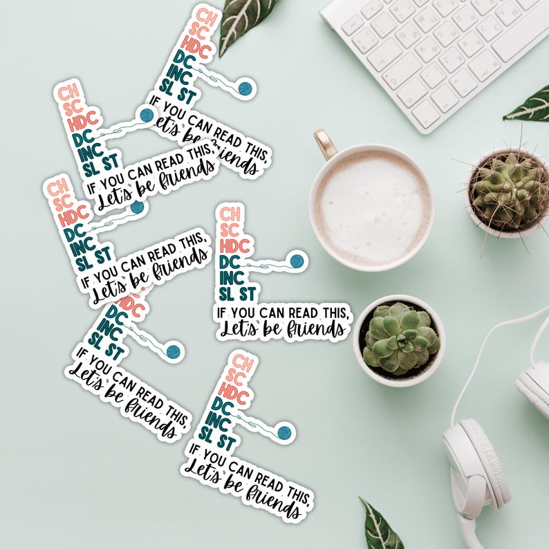 May include: A collection of white stickers with the text "IF YOU CAN READ THIS, Let's be friends" and crochet abbreviations. The stickers are scattered on a light green surface, alongside a cup of coffee, succulents, and a keyboard.