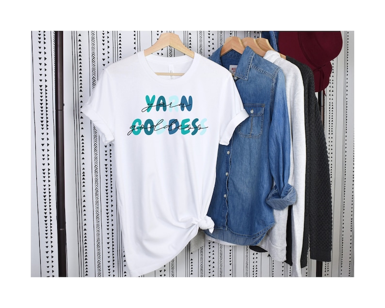 May include: White t-shirt with the text "Yarn Goddess" in blue and green lettering.