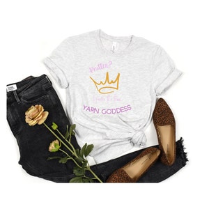 May include: A heather grey t-shirt with a gold crown and the text "Knitter? I prefer the term YARN GODDESS" in pink and purple.