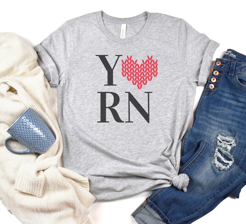 May include: A gray t-shirt with the text "Y RN" and a red knitted heart design. The heart is in the shape of a love heart.