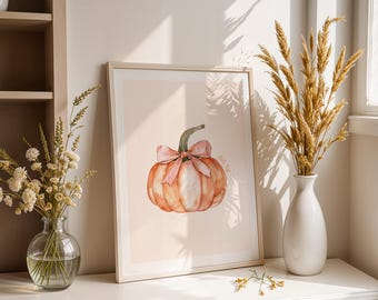 Puede incluir: Impresión en acuarela enmarcada de una calabaza naranja con un lazo rosa y un tallo verde. La impresión se muestra sobre una superficie blanca con un jarrón de trigo seco y un jarrón de flores.