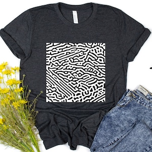 Könnte beinhalten: Ein dunkelgraues T-Shirt mit einem schwarz-weißen abstrakten Muster auf der Vorderseite. Das Muster ähnelt einem Labyrinth oder einem Netzwerk von Adern.
