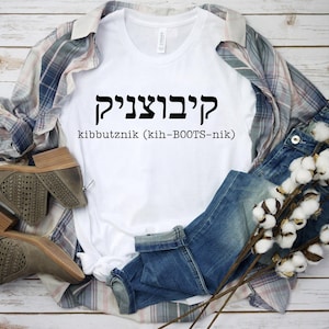 May include: White t-shirt with the Hebrew word "kibbutznik" and the English translation "kibbutznik (kih-BOOTS-nik)" printed in black.