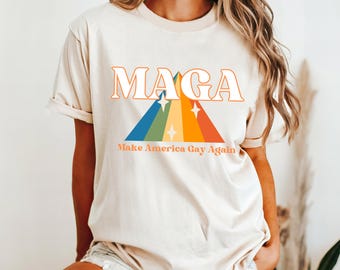 以下が含まれることがあります： レインボーのグラフィックと「MAGA Make America Gay Again」というテキストが書かれた白いTシャツです。