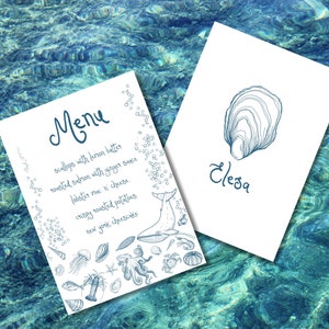 Könnte beinhalten: Eine weiße Speisekarte mit einer blauen und weißen Illustration eines Wals, eines Hummers, eines Kraken und anderer Meeresbewohner. Die Speisekarte listet Jakobsmuscheln mit Zitronenbutter, gebratenen Lachs mit Ingwer-Sauce, Hummer-Mac-and-Cheese, knusprige Bratkartoffeln und New Yorker Käsekuchen auf. Eine weiße Karte mit einer blauen Illustration einer Auster und dem Wort "Eleza" befindet sich im Hintergrund.