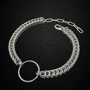 Peut inclure: Un bracelet en maille argentée avec un grand anneau argenté. Le bracelet est composé d'anneaux métalliques entrelacés et se ferme à l'aide d'un fermoir.