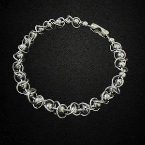 Może przedstawiać: Srebrna bransoletka z łańcuszkiem i zapięciem na zatrzask. Bransoletka wykonana jest z małych, okrągłych koralików połączonych ze sobą w skomplikowany wzór.