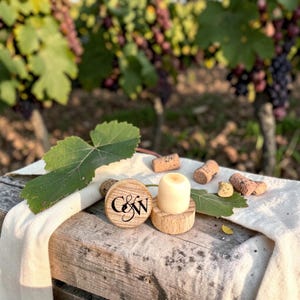 Peut inclure: Un bouchon de bouteille rond en bois avec les lettres G&W imprimées en noir sur le dessus. Le bouchon possède un insert cylindrique de couleur claire et est accompagné de plusieurs petits morceaux de liège naturel et d'une feuille de vigne.