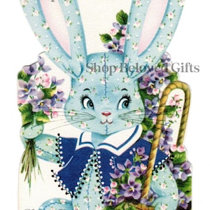 以下が含まれることがあります： 花柄の耳と体を持つ青いイースターバニーのヴィンテージイラスト。バスケットと花を持っています。「Shop Beloved Gifts」の文字が見えます。