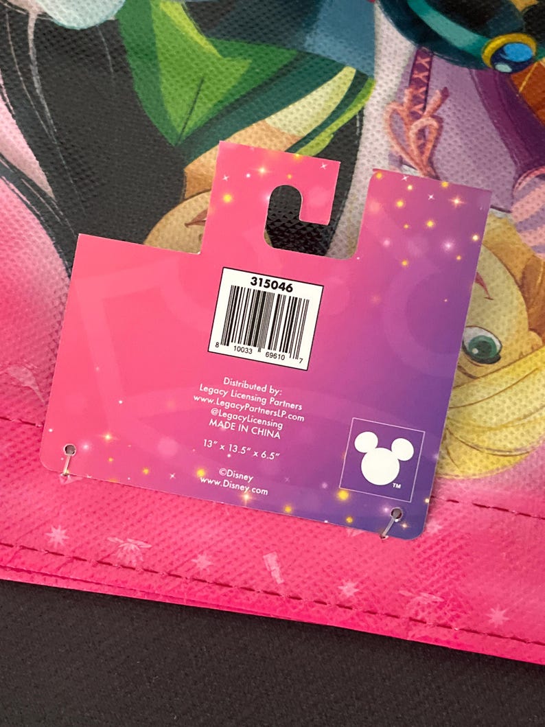 May include: A pink and purple Disney-themed tote bag with a tag. The tag has the number "315046" and the Disney logo. The bag measures 13" x 13.5" x 6.5".