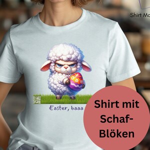 Könnte beinhalten: Hellblaues T-Shirt mit einem Cartoon-Schaf, das ein verziertes Osterei hält. Das Schaf hat einen wütenden Gesichtsausdruck. Auf dem Shirt steht "Easter, baaa". Das Shirt hat auch den Text "Shirt Magic".