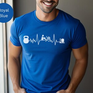 Könnte beinhalten: Königsblaues T-Shirt mit weißer Grafik eines Kettlebells, Rudergeräts, Heimtrainers und Hantelscheiben in einem Herzschlag-Design. Das Shirt hat eine einfarbige königsblaue Farbe.