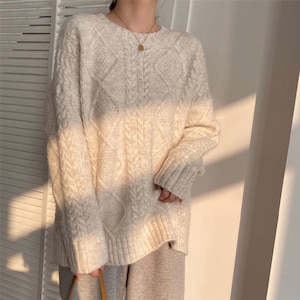 Puede incluir: Un suéter de punto de cable de color crema, de corte holgado y mangas largas.