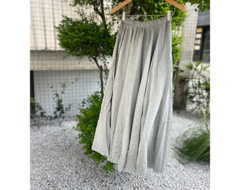 May include: A light gray maxi skirt with a gathered waist and a flowing silhouette. The skirt is made of a soft, lightweight fabric and has a relaxed fit.