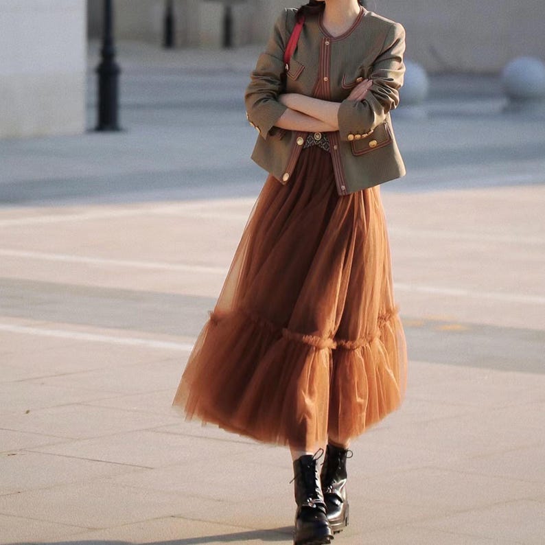 May include: A woman wearing a brown tulle skirt with multiple layers of ruffles, a green military-style jacket with gold buttons, and black combat boots.