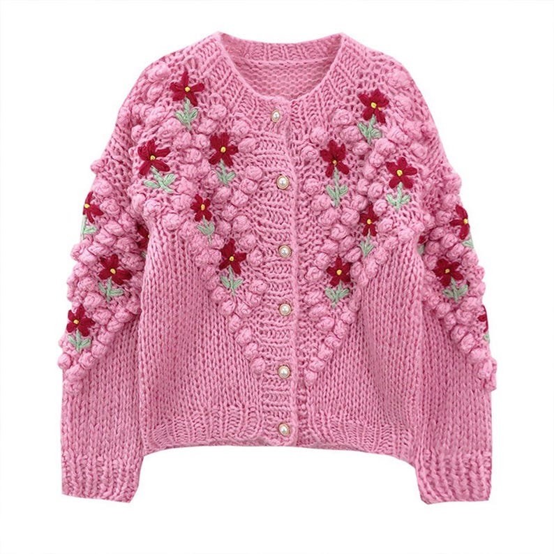 Puede incluir: Un c&aacute;rdigan de punto rosa con un dise&ntilde;o bordado floral. El c&aacute;rdigan tiene cierre de botones y un punto texturizado y abultado.