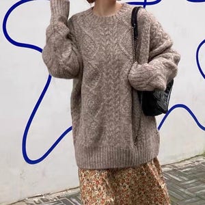 May include: A brown cable knit jumper with a loose fit and long sleeves. The jumper is worn over a floral skirt.