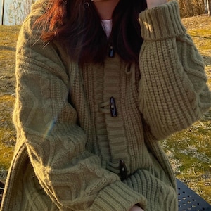 Könnte beinhalten: Ein grüner Strickpullover mit Kapuze und einer Reihe von Holz-Knöpfen.