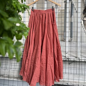 May include: A long, terracotta-colored skirt with a gathered waistline. The skirt is made of a lightweight fabric and has a flowing silhouette.