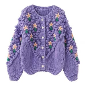 Puede incluir: Un c&aacute;rdigan de punto morado con un dise&ntilde;o floral y botones de perla. El c&aacute;rdigan tiene un punto texturizado, abultado y un ajuste holgado.