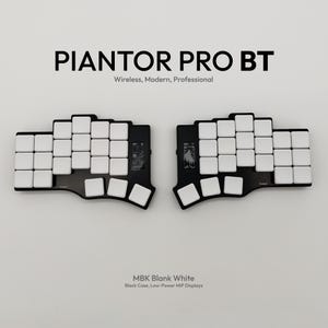 Könnte beinhalten: Eine geteilte ergonomische Tastatur mit weißen Tastenkappen und einem schwarzen Gehäuse. Die Tastatur ist mit "PIANTOR PRO BT" und "MBK Blank White" beschriftet. Das Design umfasst ein Low-Power-MiP-Display und wird als kabellos, modern und professionell beschrieben.