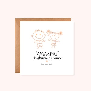 May include: A white greeting card with a brown envelope. The card has orange line drawings of two stick figures and the words "AMAZING tiny human tamer" with a heart symbol. The text "Love from Noah" is below the phrase.